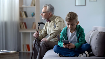 Boy using mobile phone, upset granddad sitting aside, internet addiction concept
