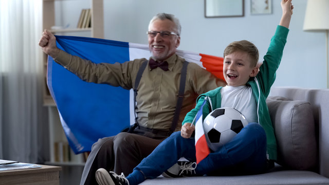 Old man holding French flag, together with boy rejoices victory of football team