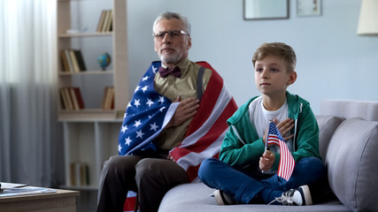 Patriotic old man holding American flag, listening national anthem with grandson - obrazy, fototapety, plakaty