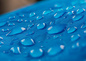 Water drops on waterproof nylon fabric. Macro detail view of texture of blue woven synthetic waterproof clothing. Waterproof fabric with water drops. Rain Drops on Water Resistant Textile