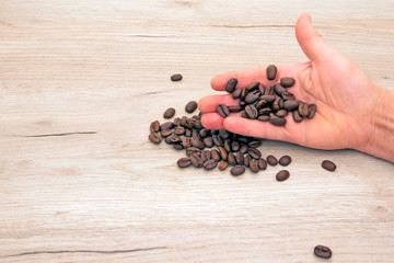 Human hand holding roasted coffee beans, other beans scattered on a wooden board