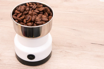 Coffee grinder with whole roasted coffee beans placed on a wooden surface