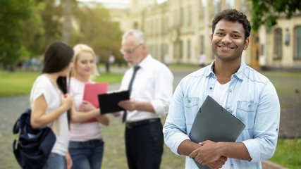 Fototapeta premium Happy Hispanic student standing near college and smiling at camera, education