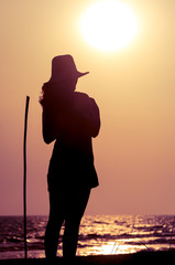 The silhouette woman with hat in beach at sunset. Female looking sea.