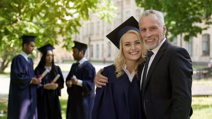 Female graduate hugging dad and smiling into camera, successful future, career