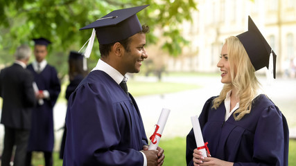 Couple of graduate students with diplomas talking and smiling to each other