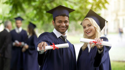 Male and female graduates showing diplomas and smiling, complete high education