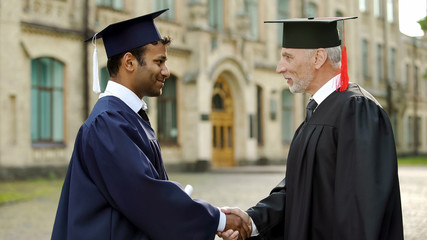 Eminent professor giving diploma to male student shaking hand, successful future