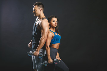 Obraz premium Sporty young sexy couple isolated over black background with dumbbells.