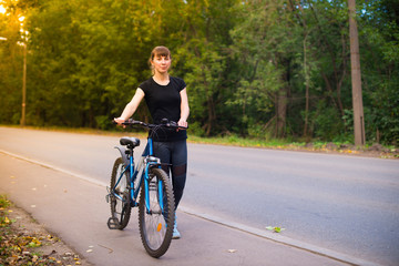 young beautiful girl leads the bike on the sidewalk