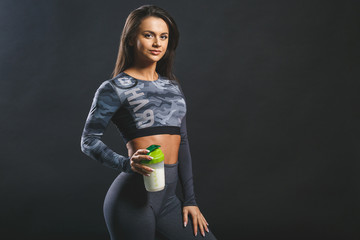 Attractive young woman with protein shake bottle isolated over black background.