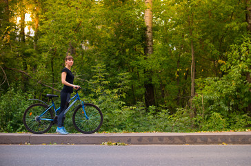 Fototapeta premium Young beautiful athletic girl in sportswear posing on a blue bike. Trees on the background.