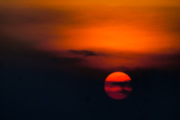 red orange circle Sun behind cloud in sunset time twilight evening . Landscape with red sun setting behind dark clouds and silhouette of hills 