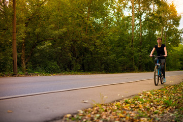 Obraz premium young beautiful girl in sportswear rides a blue bike on the sidewalk. Trees on the background.