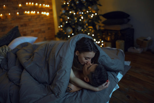 Young lovers are lying in bed during lovemaking on background of the Christmas tree.