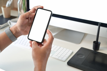 Unrecognizable man using mobile phone on desk in office. Blank screen smart phone for graphic montage