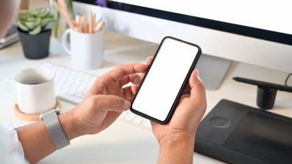 Man holding a mobile phone with white blank screen over the desk in the office