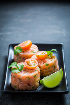 Salmon tartare with lime and cherry tomatoes on concrete table