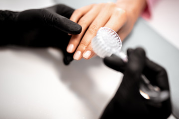 Close up of the professional manicurist in rubber gloves cleaning the nails of his client while using special nail brush