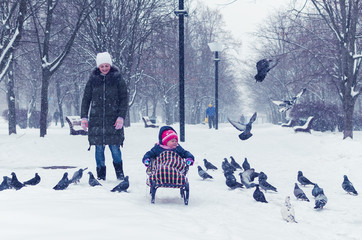 Mom pulls daughter on sled in winter park in snowfall