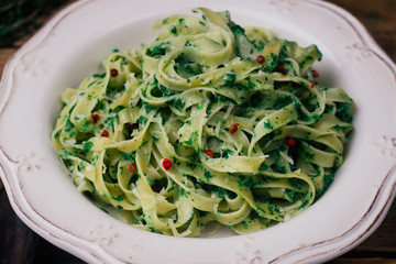 Spinach Fettuccine. Vegan pasta with spinach (Spinach Fettuccine Alfredo Pasta) on a white plate. Old wooden background
