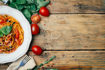 Spaghetti pasta with tomato sauce, parmesan and basil on a white plate. The classic tomato spaghetti: vegetarian tomato basil pasta. Old wooden background. Copy space.