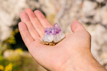 druse of natural untreated violet crystals of amethyst on a piece of rock lies on the palm of your...