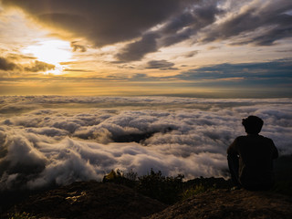 Obraz premium Silhouette People Sit on the cliff with beautiful sunrise sky on on Khao Luang mountain in Ramkhamhaeng National Park,Sukhothai province Thailand