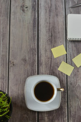 Wooden office desk table with a notebook, a handle, a cup of coffee and a flower pot. Top view with copy space.