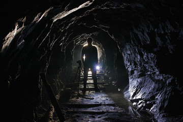 Naklejka premium Black silhouette of a photographer with a camera on a tripod in an old abandoned mine.