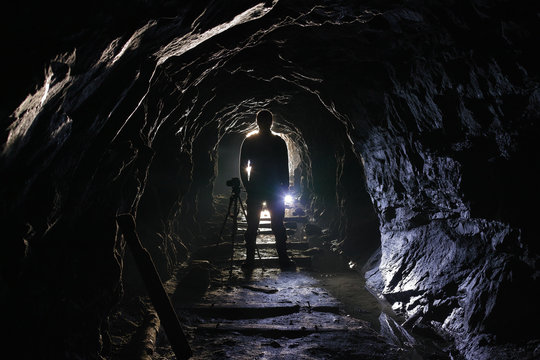 Black silhouette of a photographer with a camera on a tripod in an old abandoned mine.