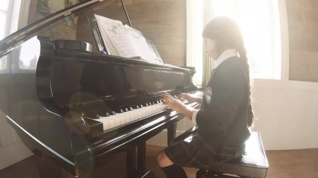 Little girl studying piano in a classroom. Sunlight entering the room. 4k