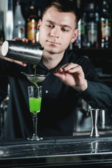 bartender making Green Alcoholic Cocktail pouring fluid into glass.