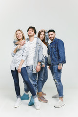 Group of smiling friends in fashionable jeans. The young men and woman posing at studio. The...
