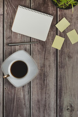 Wooden office desk table with a notebook, a handle, a cup of coffee and a flower pot. Top view with copy space.