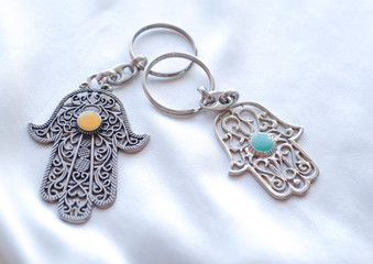 Two key rings in the form of Fatima Hand on a white silk background. Ancient symbol and traditional modern tourist souvenir of Tunisia.