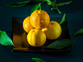 Juicy tangerine and orange mandarin with leaves on black plate. Fruits concept.