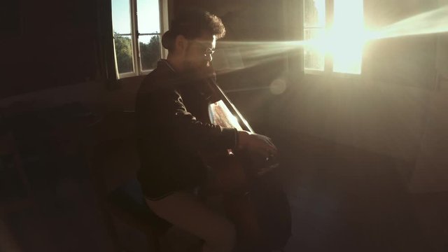 Hispanic cellist practicing classical music on cello at a beautiful sunset in a classroom. 4k