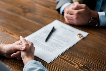 partial view of lawyer and client sitting at table with divorce decree and wedding rings - obrazy, fototapety, plakaty