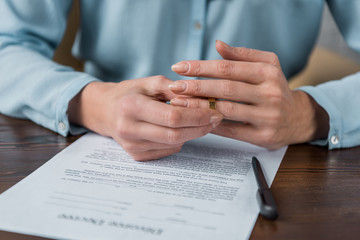 cropped shot of woman taking off wedding ring and divorce decree on table - obrazy, fototapety, plakaty