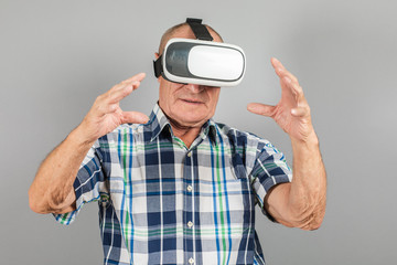 Grandfather looks into VR glasses, hand gestures, on a gray background.