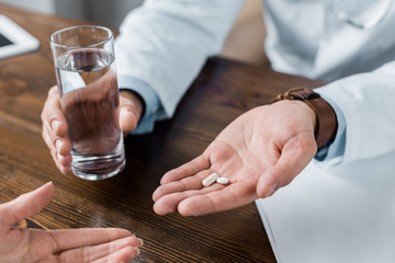 cropped shot of doctor giving pills and water to patient at office