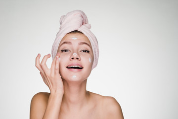 smiling beautiful girl with a pink towel on her head applying white cream on her face