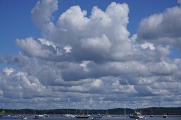 Fototapeta na wymiar Castine, Maine, USA: Small boats in the waters of Penobscot Bay, under a blue sky with dramatic white clouds overhead.