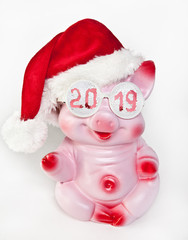 Cheerful pink pig in a new year's cap and glasses with the inscription 2019 sits on a white background.