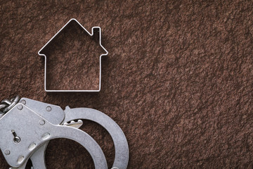 Handcuffs and a figure in the shape of a house on stone surface with copy space. Concept on real...