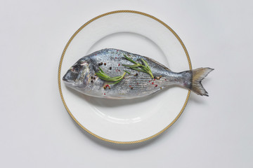 top view of uncooked fish with rosemary and pepper on plate