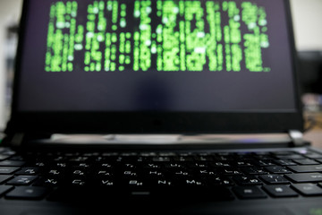 a hacker with a hood over a screen with binary code