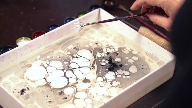 Splashing white color. Ebru is art of painting on liquid water surface. Paper marbling. Woman drawing with brush and black paint. Close up hand. Hobby, arts, culture concept