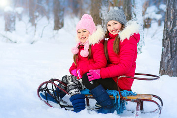 two cute little girls 6-10 years old sledding in the winter forest